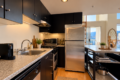 Modern kitchen with black cabinets, stainless steel appliances, granite countertops, and a city skyline seen through large windows.