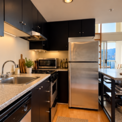 Modern kitchen with black cabinets, stainless steel appliances, granite countertops, and a city skyline seen through large windows.
