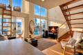Modern loft living room with large city-view windows, a wooden staircase, and a fireplace beside a TV.