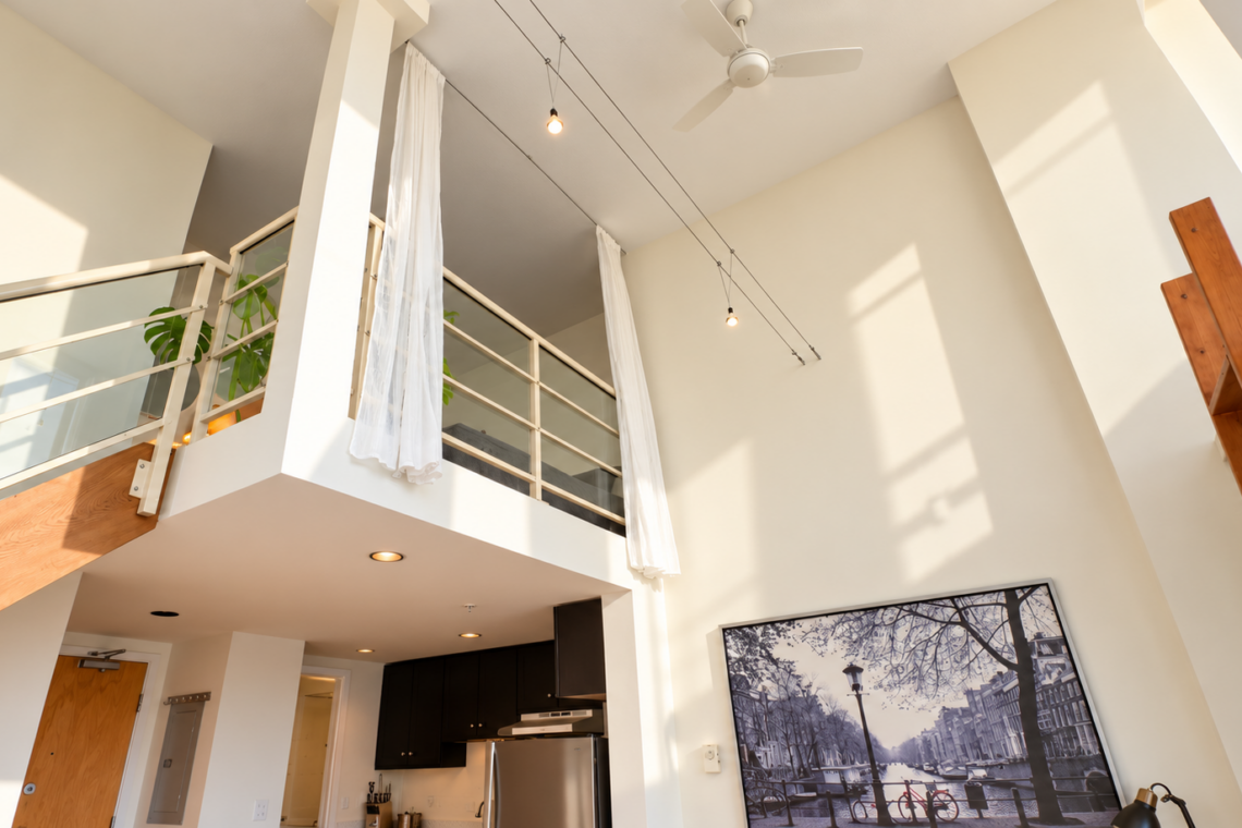 Open-concept loft with mezzanine, white drapes, and a wooden staircase leading to the upper level.