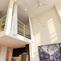 Open-concept loft with mezzanine, white drapes, and a wooden staircase leading to the upper level.