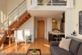Open-plan living space with a wooden staircase, white lounge chair, glass side table, gray sofa, and a kitchen island.