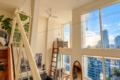 Bright modern loft with large windows and city views, featuring a wooden ladder, plant, and bed nook on the left side.