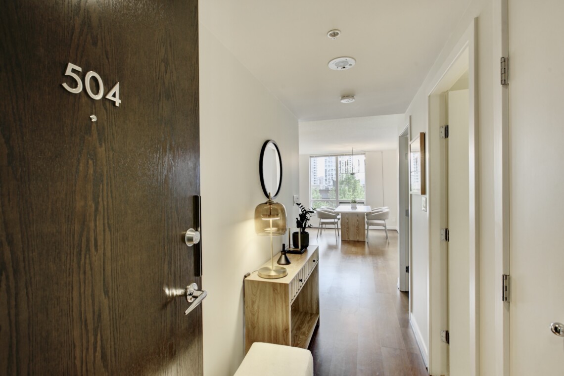 Door with 504 plaque opens to a bright hallway leading to a dining nook and living area in a modern apartment.
