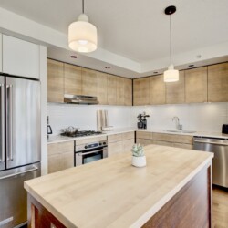 Modern kitchen with stainless steel refrigerator, white countertop and light wood cabinets surrounding a large island.