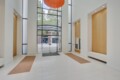Bright modern lobby with tall glass entrance, large orange circular light, white walls, and wood-panel niches.