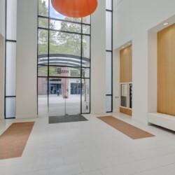 Bright modern lobby with tall glass entrance, large orange circular light, white walls, and wood-panel niches.