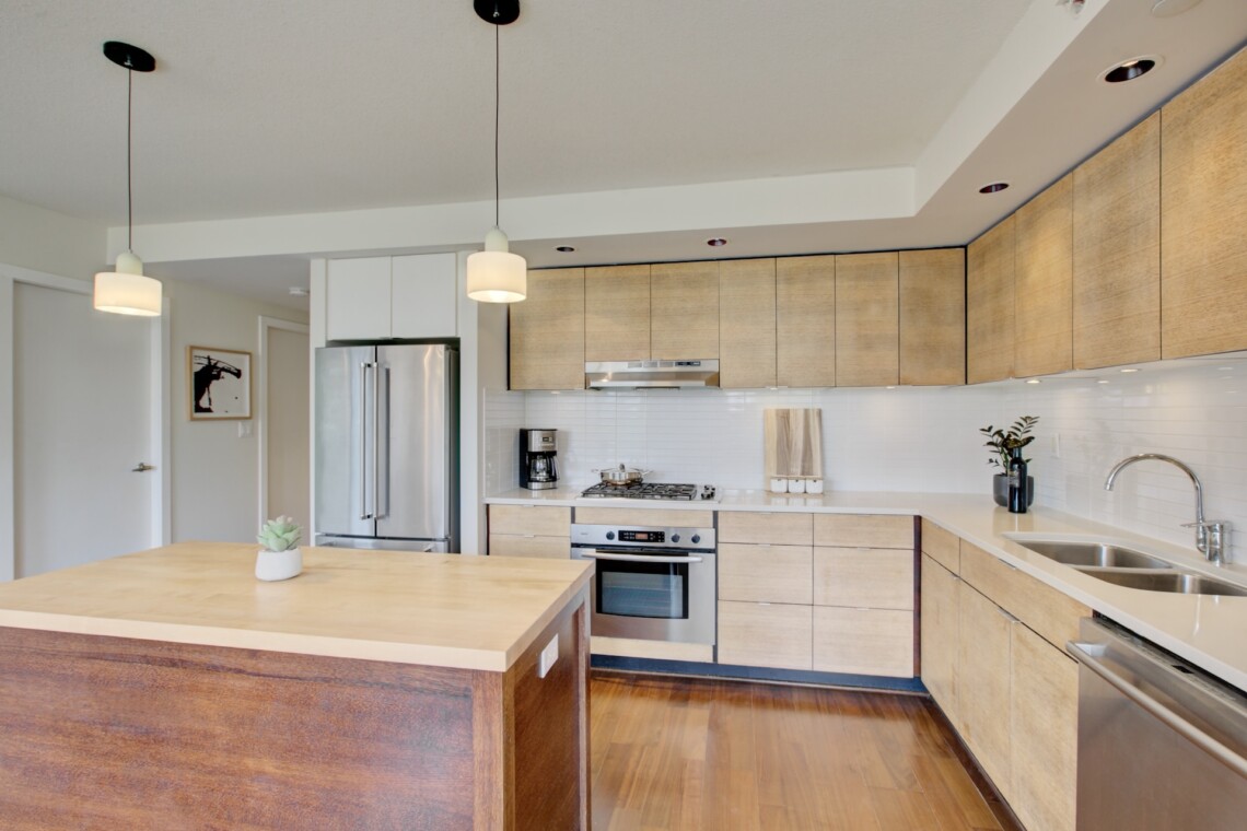 Modern kitchen with wood cabinets, stainless steel appliances, white tile backsplash, and an island centerpiece.