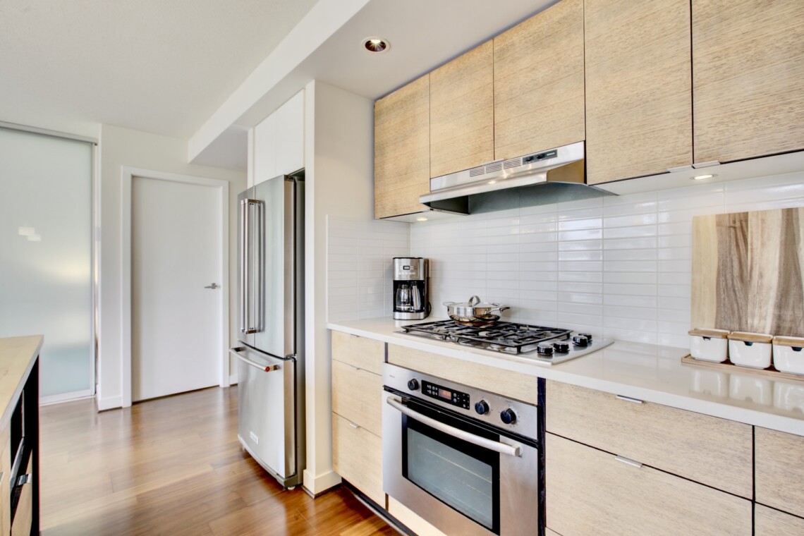 Modern kitchen with stainless fridge, white cabinetry, and a gas range under a range hood.