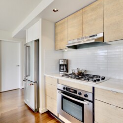 Modern kitchen with stainless fridge, white cabinetry, and a gas range under a range hood.