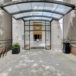Front entrance of a modern building with a curved glass canopy, double doors, and the number 1055 above the doorway.