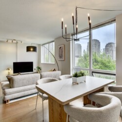Bright open-concept living room with a white dining table and beige chairs, overlooking a cityscape through large windows.