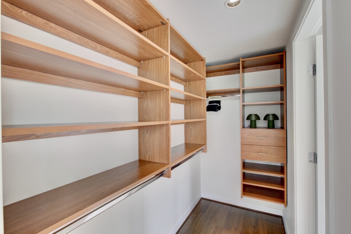 Walk-in closet with light wood open shelves along two walls and a set of drawers at the far end.