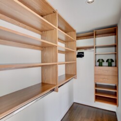 Walk-in closet with light wood open shelves along two walls and a set of drawers at the far end.