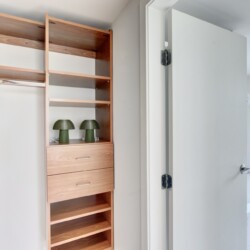 Open closet with tall wooden shelves and drawers, two green ribbed lamps on a shelf, and a doorway to a bright bathroom.