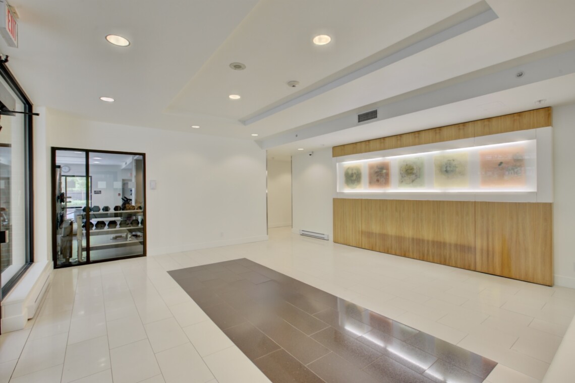 Modern building lobby with a long wooden reception desk and backlit abstract art panels on the wall