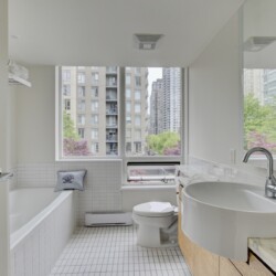 Bright modern bathroom with a white tub, toilet, and curved sink, large window showing city buildings outside