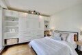 Modern white bedroom with a full wall of built-in wardrobes, open shelves, and a bed with white bedding on a wooden floor.