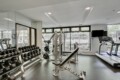 Gym with a dumbbell rack on the left, weight machines in the center, and a treadmill on the right by large windows.