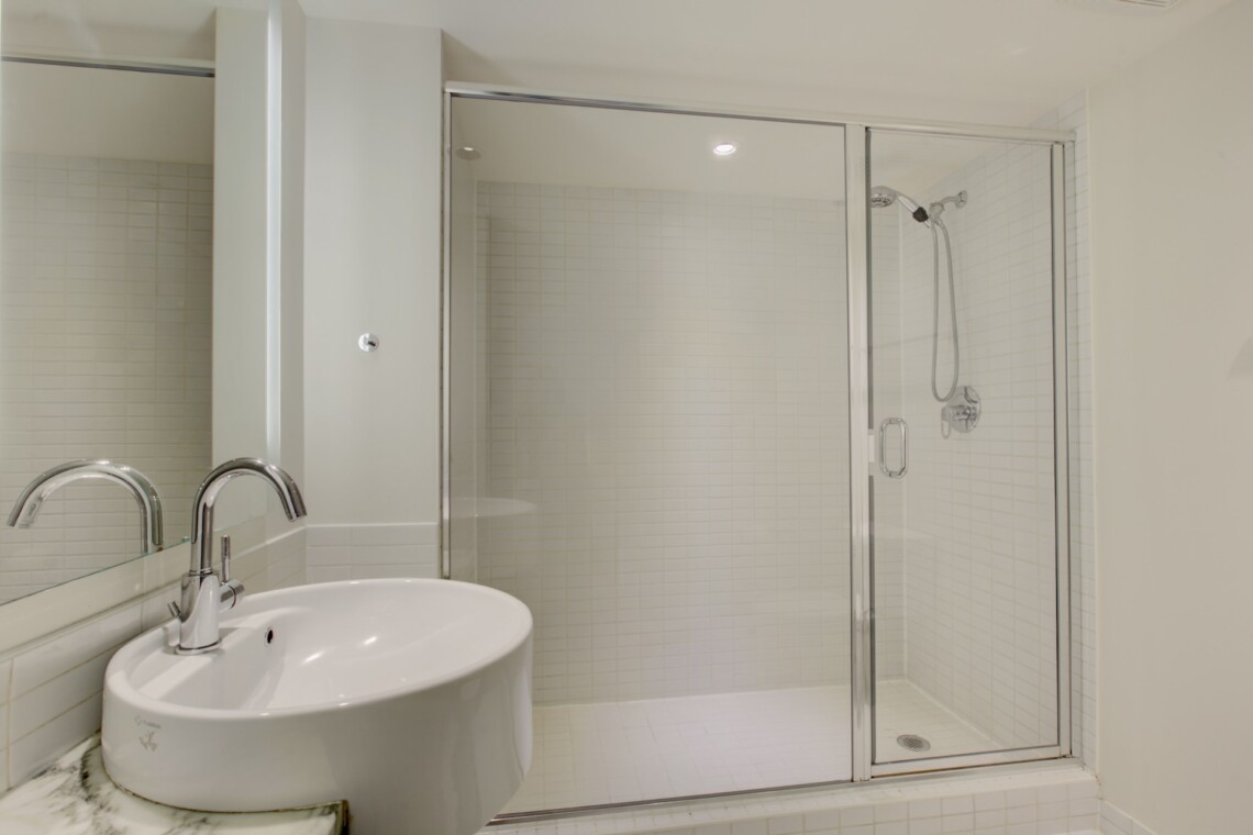 Bathroom with glass-enclosed shower, white tiled walls, and a white oval sink with chrome faucet in a clean, modern space