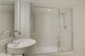 Bathroom with glass-enclosed shower, white tiled walls, and a white oval sink with chrome faucet in a clean, modern space