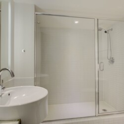 Bathroom with glass-enclosed shower, white tiled walls, and a white oval sink with chrome faucet in a clean, modern space