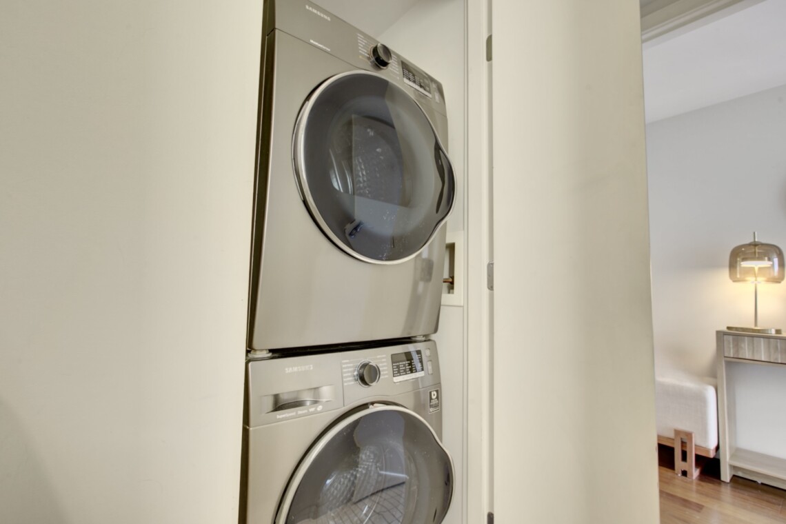 Stacked front-load washer and dryer in a laundry closet with the doors open, showing the appliances in a modern home.