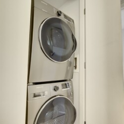 Stacked front-load washer and dryer in a laundry closet with the doors open, showing the appliances in a modern home.