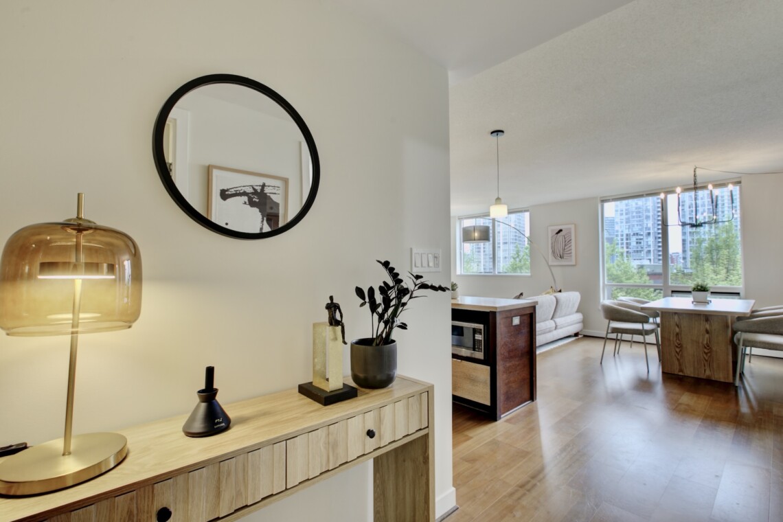 Console table with decorative objects and a gold glass lamp, mirrored by a round black-framed mirror on a pale wall reflecting art in the background