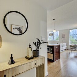 Console table with decorative objects and a gold glass lamp, mirrored by a round black-framed mirror on a pale wall reflecting art in the background