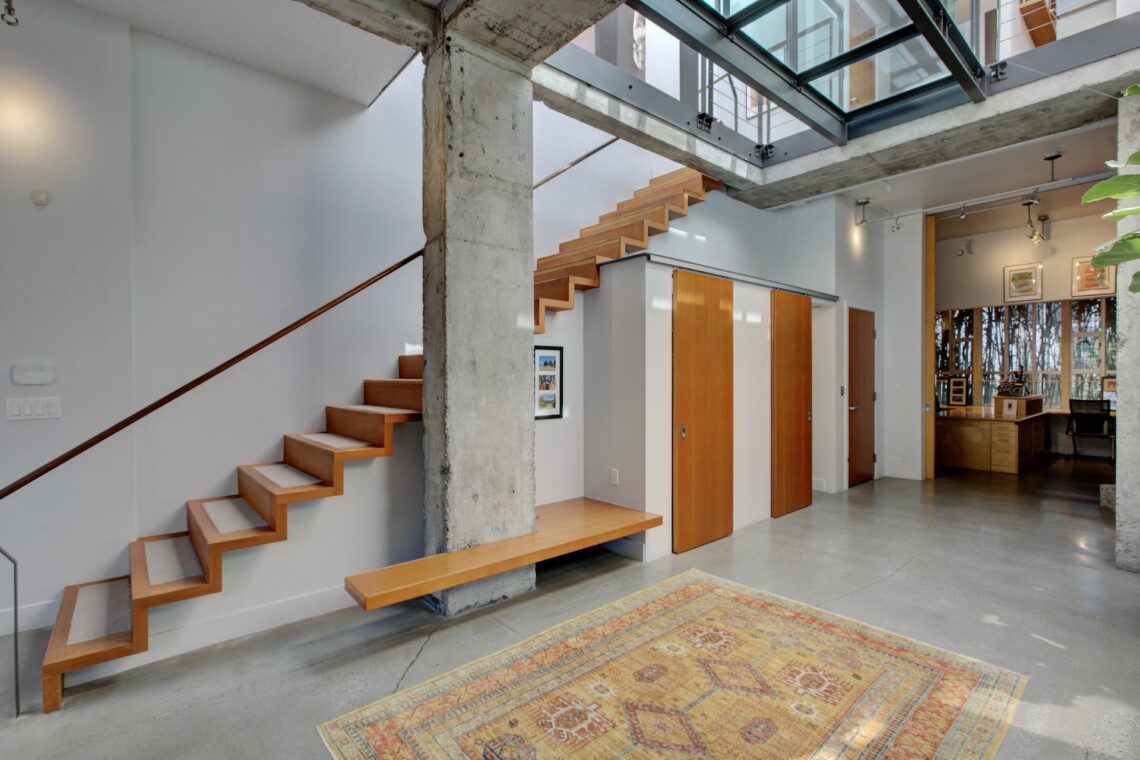 Modern interior with floating wooden stairs beside a concrete pillar and built-in bench along a gray wall.