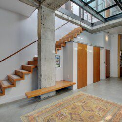 Modern interior with floating wooden stairs beside a concrete pillar and built-in bench along a gray wall.