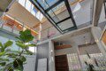 Modern multi-level interior with a glass skylight, concrete beams, metal railings, and a large leafy plant in the foreground.
