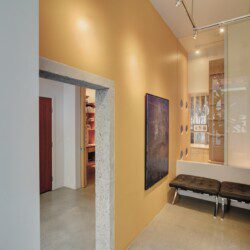 Modern interior hallway with an orange accent wall, a large chalkboard, and black tufted benches along a glass partition.