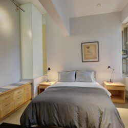 Bedroom with a centered bed, gray bedding, two wooden nightstands with lamps, and a framed drawing above the headboard.
