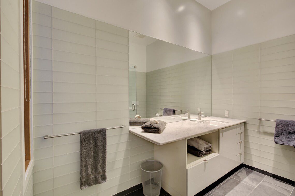 Contemporary bathroom with a white double-sink vanity, marble countertop, large mirror, and gray towels.