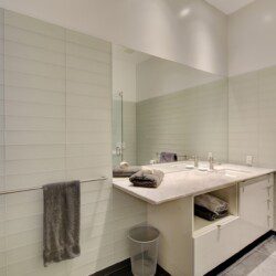 Contemporary bathroom with a white double-sink vanity, marble countertop, large mirror, and gray towels.