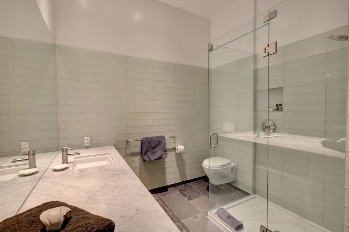 Contemporary bathroom with a double-sink vanity, marble countertop, and a glass-enclosed shower.