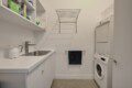Laundry room with a sink, counters, and white cabinets, plus a stacked washer/dryer on the right and a shelf of cleaners above.