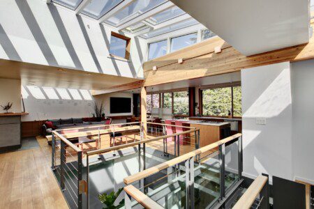 Bright open-concept living area with glass railing and skylights overhead, casting striped shadows on the walls and floor.