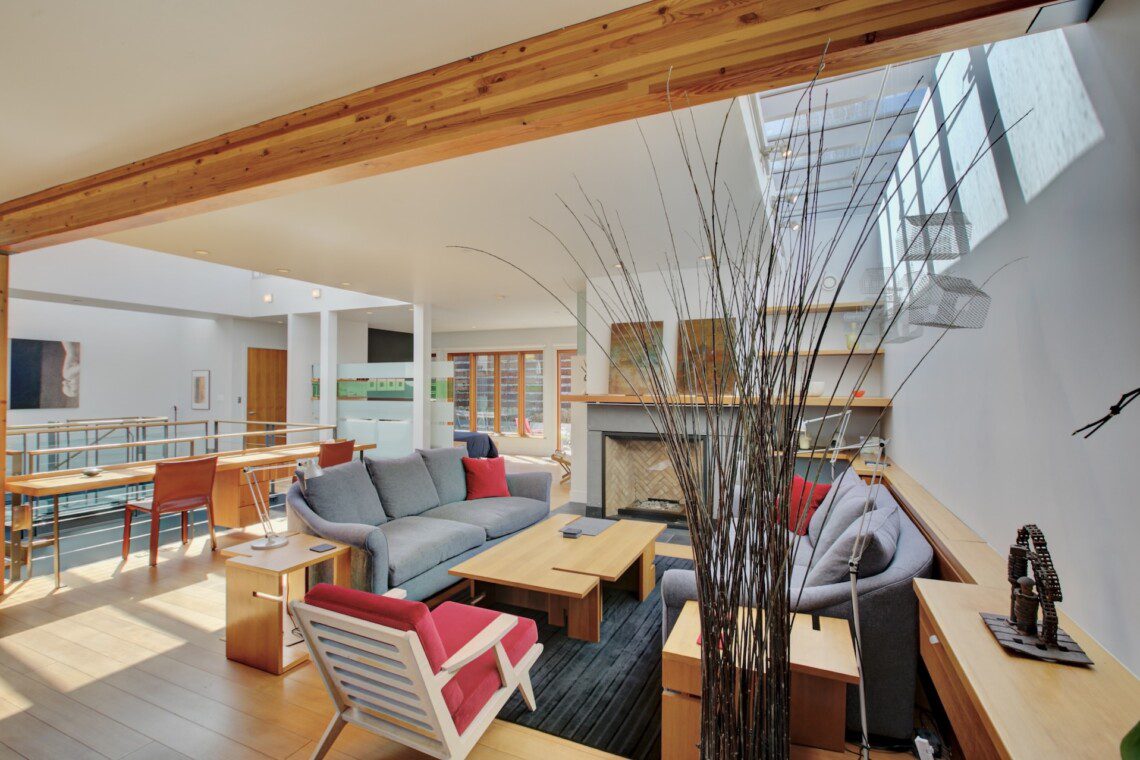 Bright open-concept living area with a gray sectional, red accents, and a wooden coffee table by a fireplace.