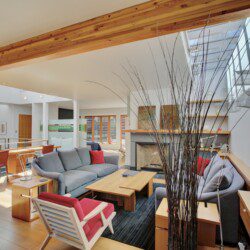 Bright open-concept living area with a gray sectional, red accents, and a wooden coffee table by a fireplace.