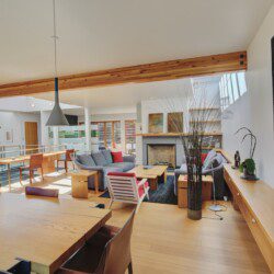Open living space with wooden floors, ceiling beams, a gray sectional sofa, and a fireplace in the center