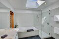 Bright modern bathroom with a white tiled bath and glass-enclosed shower under a skylight.