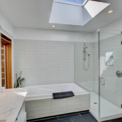 Bright modern bathroom with a white tiled bath and glass-enclosed shower under a skylight.