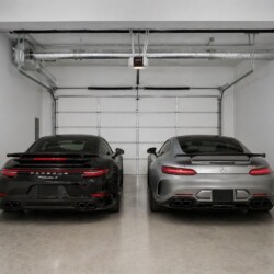 Black Porsche 911 Turbo S and silver Mercedes-AMG GT parked side by side in a clean, empty garage.