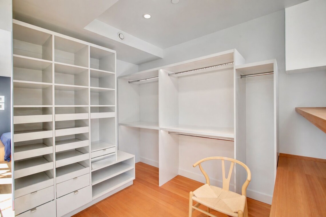 Walk-in closet with white modular shelves, drawers, and hanging rails on a light wooden floor.