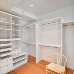 Walk-in closet with white modular shelves, drawers, and hanging rails on a light wooden floor.
