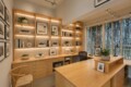 Bright wooden home office with built‑in shelving, warm lighting, books, and potted plants.