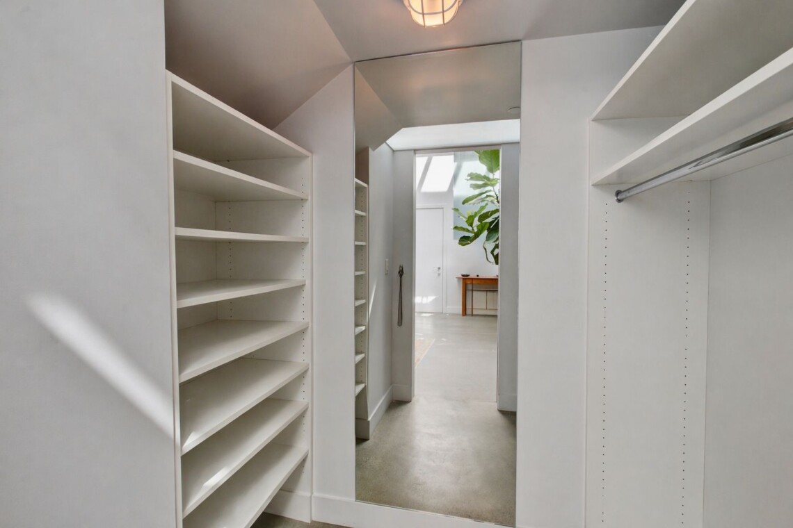 Walk-in closet with white built-in shelves and a full-length mirror reflecting a bright room with a potted plant.